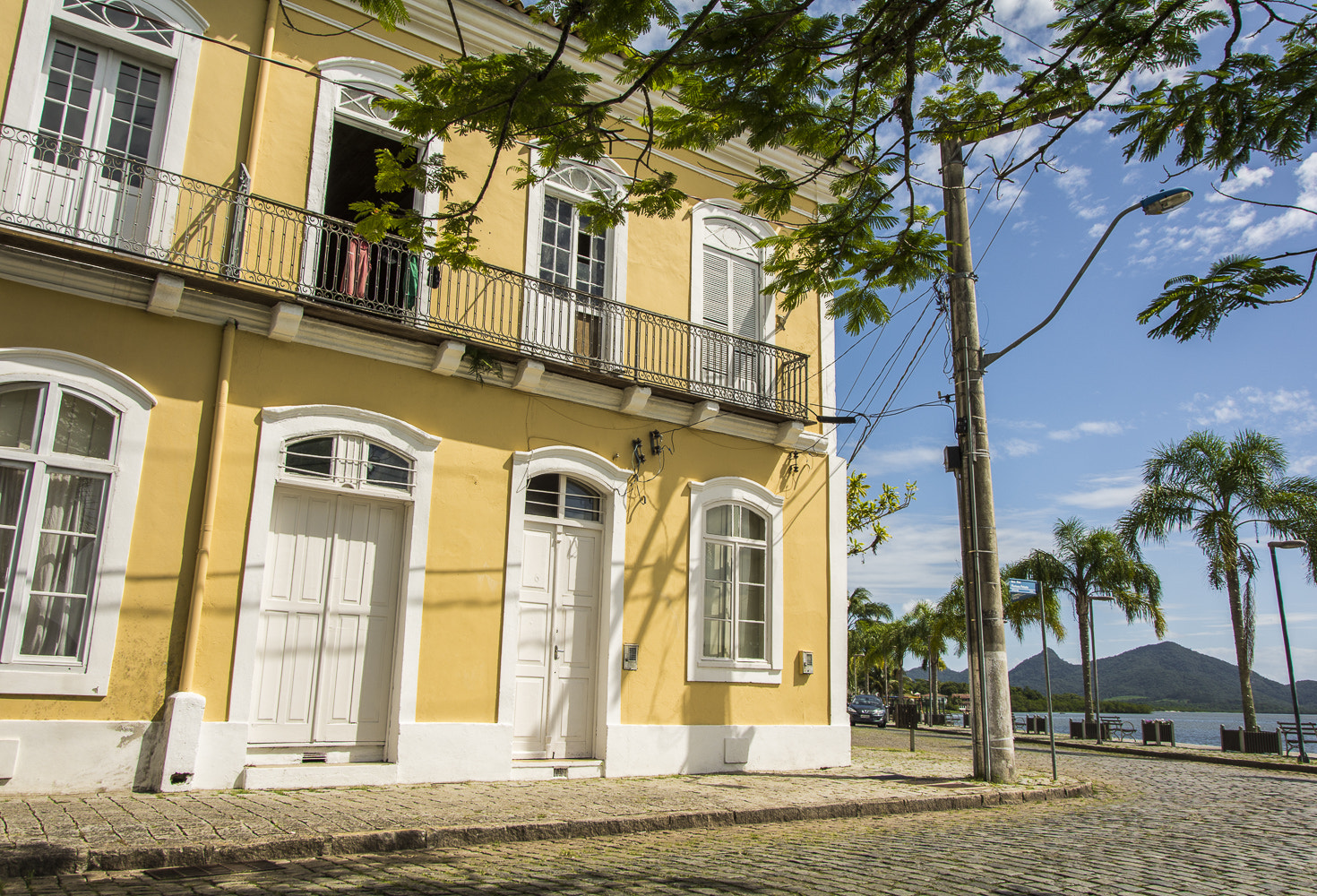 Casarão colonial amarelo em rua de paralelepípedos no centro histórico de São Francisco do Sul, cidade litorânea de Santa Catarina, com a baía ao fundo